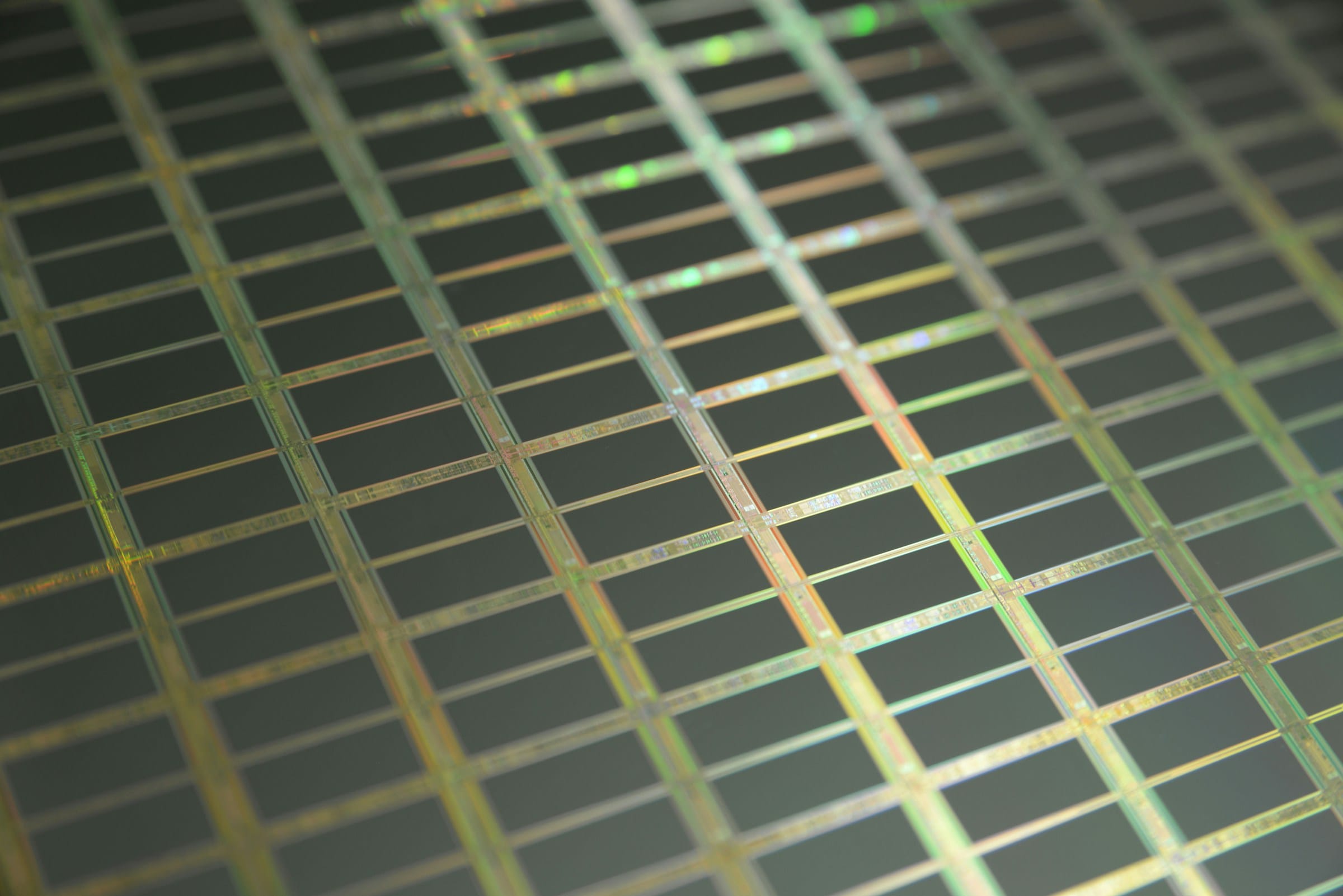 Macro view of a silicon wafer showing a grid of rectangular chips separated by fine gold and green lines.